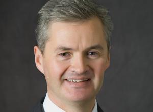 A portrait of Geoffrey Austin in a suit with a dark grey background