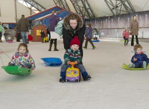 Toddlers playing on ice rink with sledges and toys