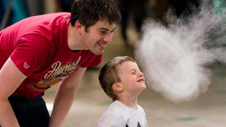 A young boy facing the vapour rings and closing his eyes with his guardian stood behind him