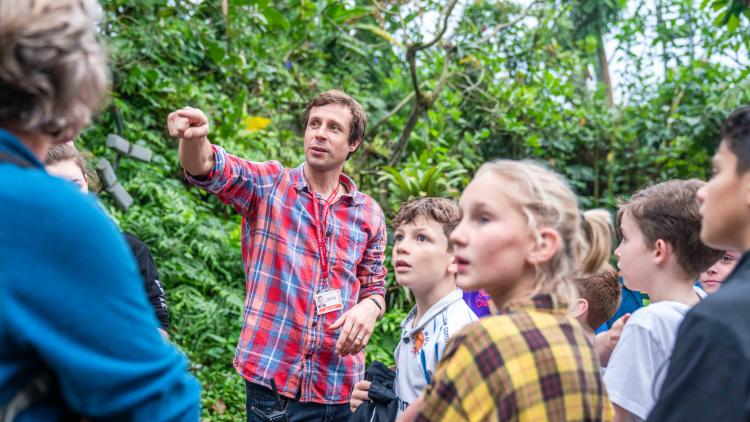 A group of school pupils standing looking in the direction of the teacher who is pointing 