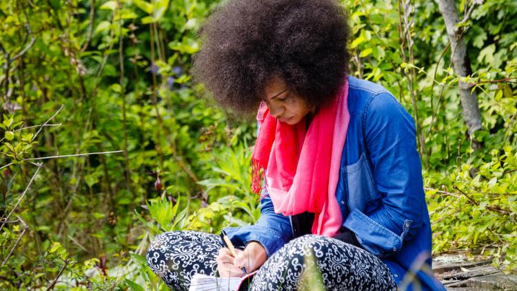 Women sat outside writing in a notebook