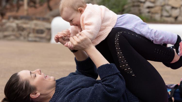 Mother on her back with baby balancing on her knees