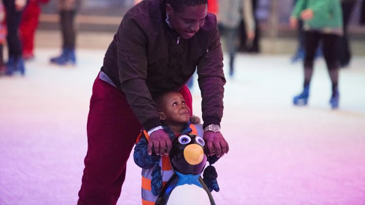 Father helping young son ice skate with penguin aid