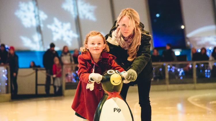 Mum and daughter holding onto penguin ice skate aid