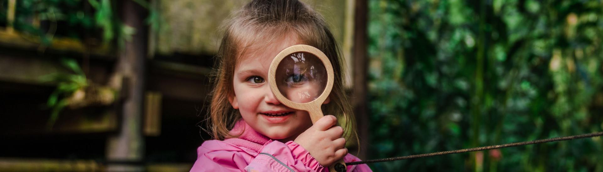 Young girl in a pink coat holding a magnifying glass up to her eye