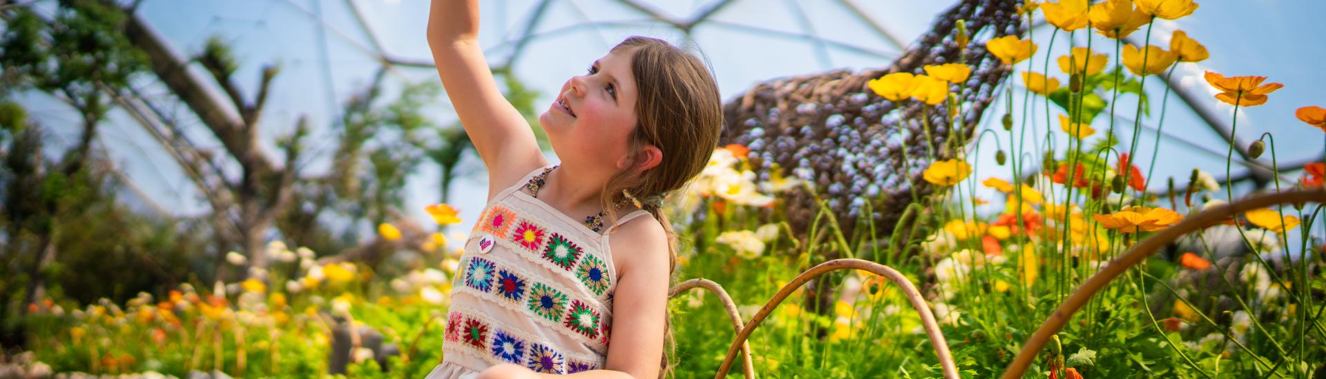 Girl holding wooden painted egg sat next to yellow and orange poppies in the Eden Project's Mediterranean Biome